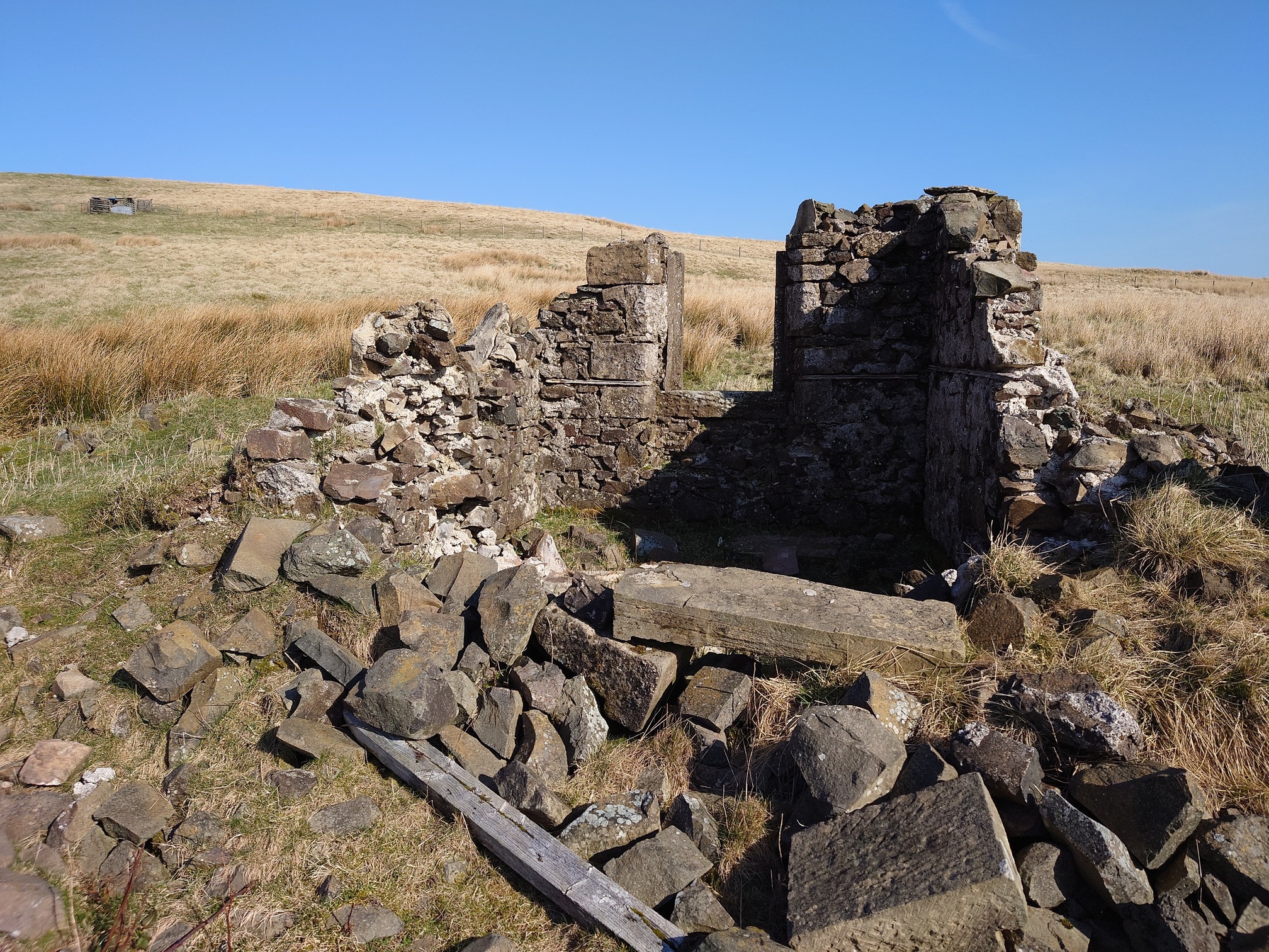 A view of the same ruin from inside, large blocks of stone and a lintel lie on the ground. Beyond, a section of wall with the remains of a window