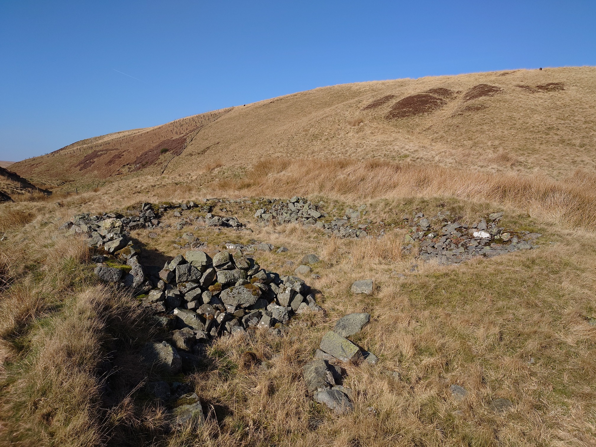 Stones piled in a large rectangular shape, sitting in the grass at the foot of a rounded hill