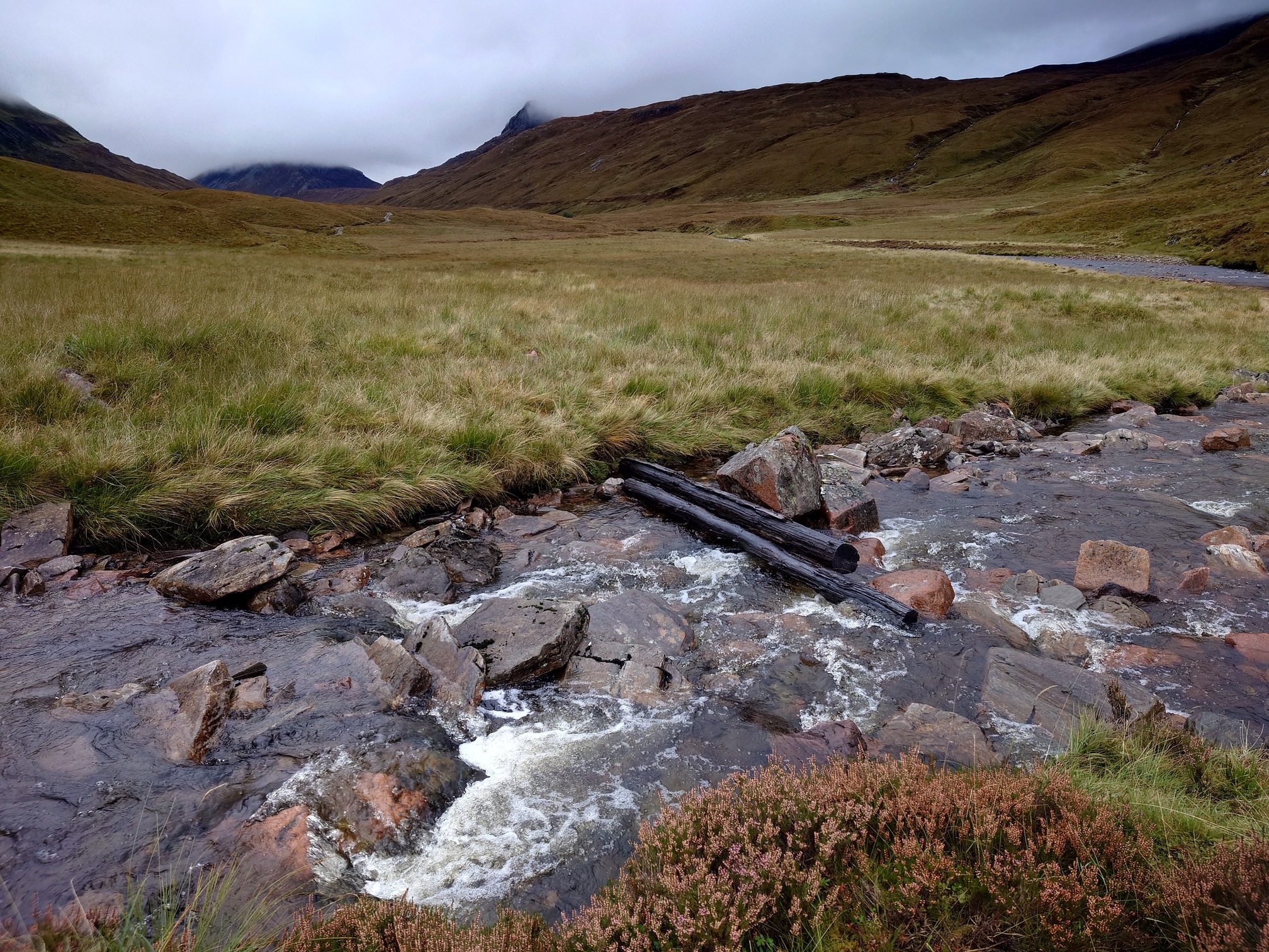 A rocky burn crossing, two old pieces of timber are the remains of what was a footbridge