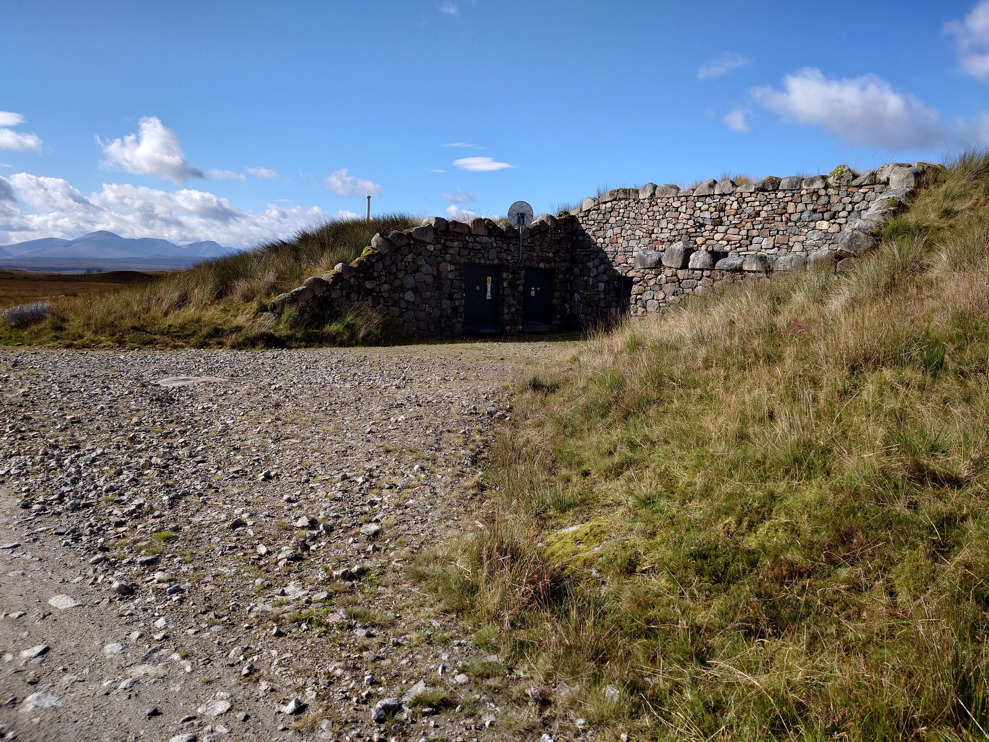 A stone wall with doors in a grassy bank with a gravel yard is actually an electricity substation 