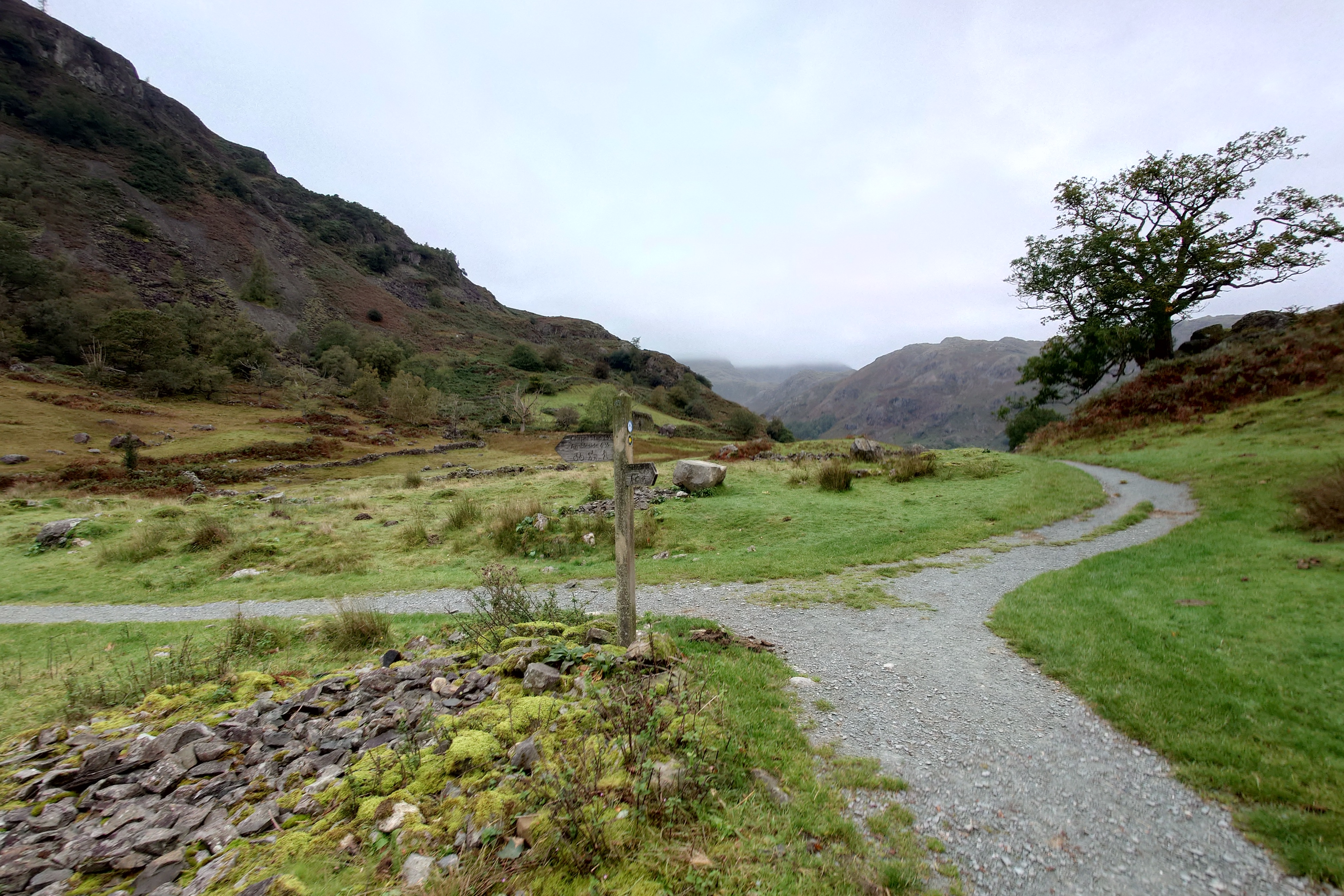 The gravel path splits here on the valley floor, with steep slopes rising off to the left of the pictures. A wooden directional sign gives the way