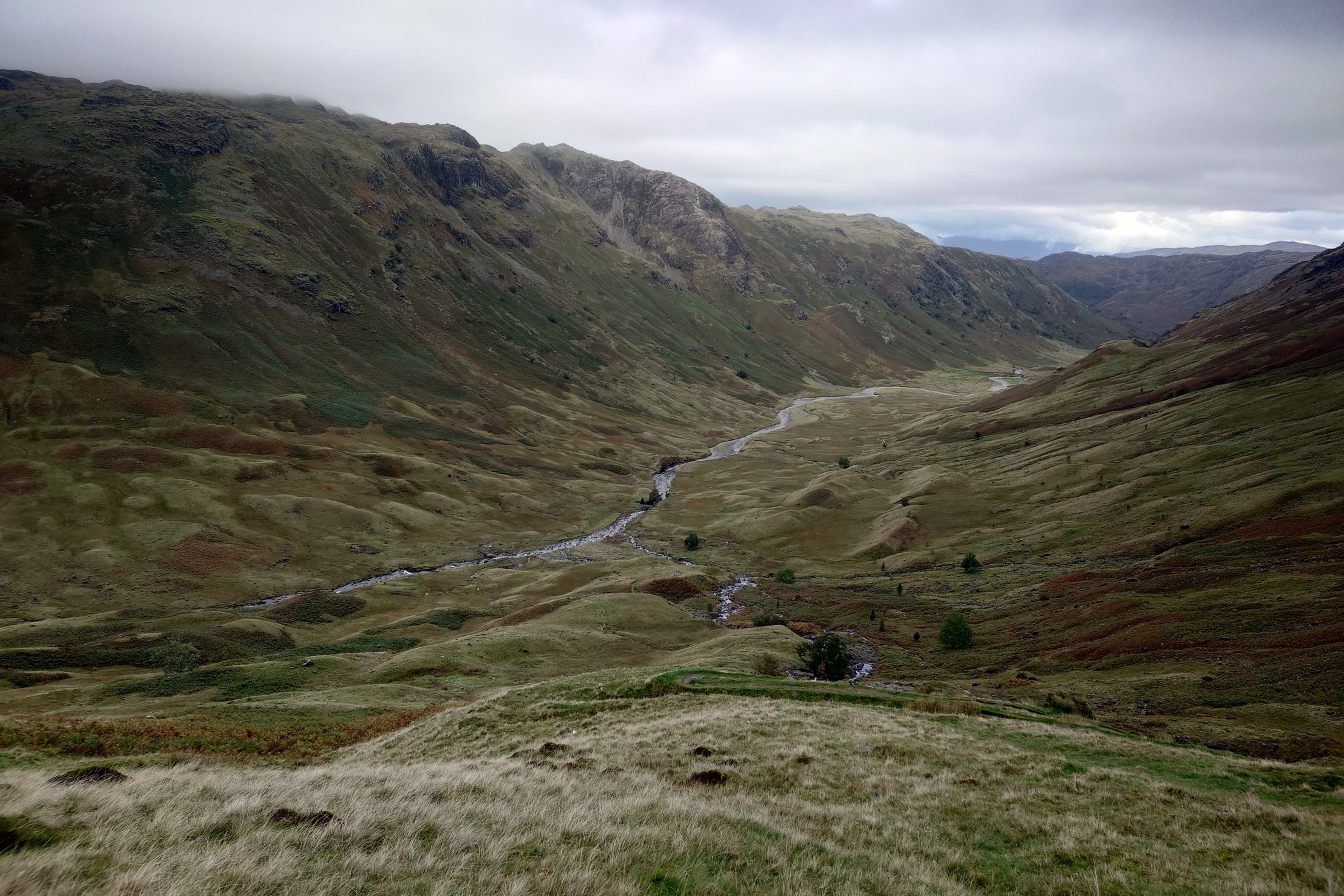 Langdale, with bigger, steeper slopes and a larger river winding down it. The tops of the hills are knobbly rocks. it is a vast landscape.
