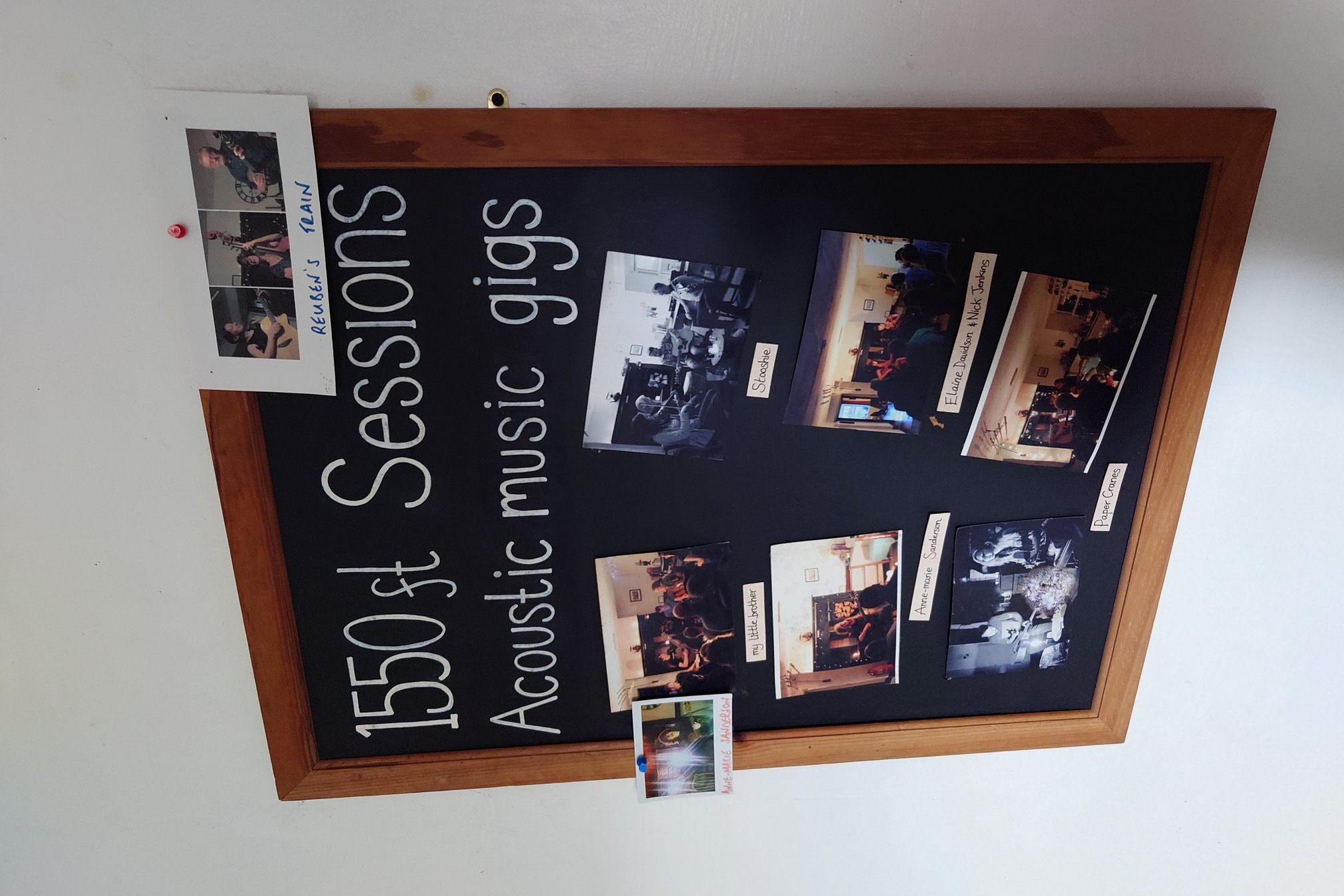 A chalkboard reads 1550 ft Sessions Acoustic Music Gigs with photographs of musicians who have played at the hostel