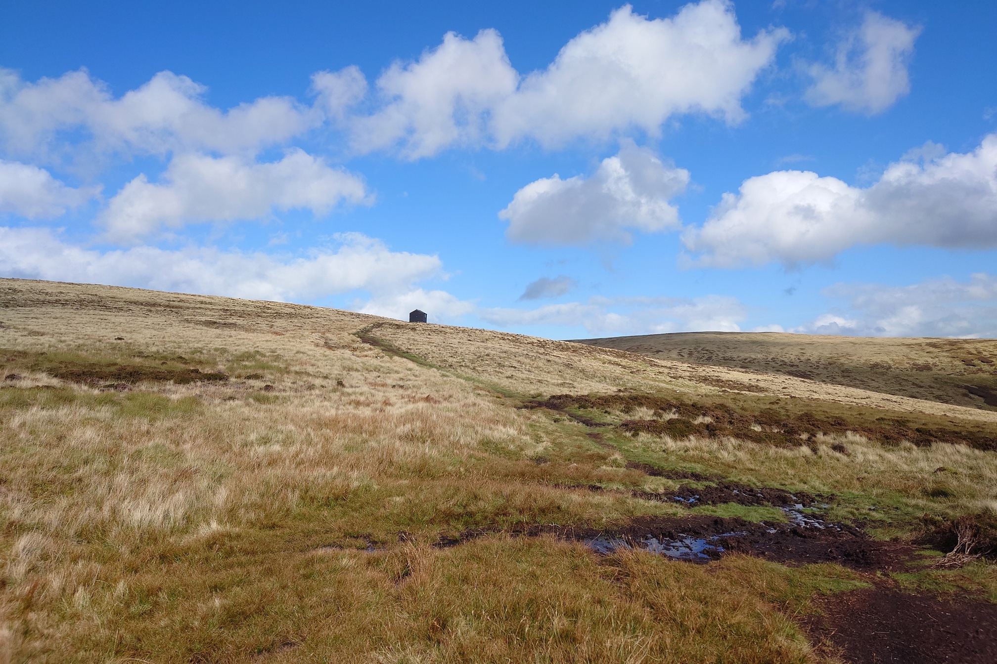 Up the grassy slope, a square hut stands on the horizon