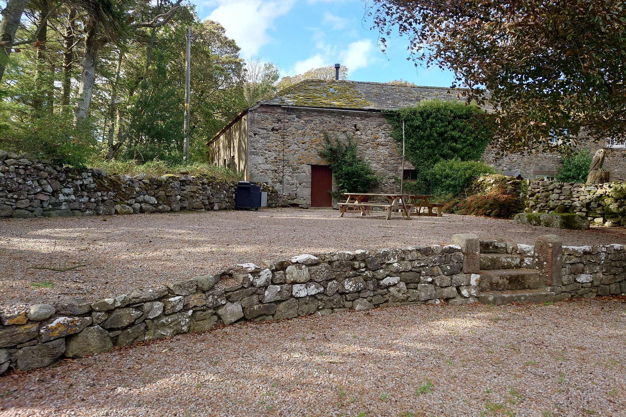 Hudcsale Camping Barn, an old agricultural barn now looking lovely with a very neat gravel area in front, trees either side and a red door