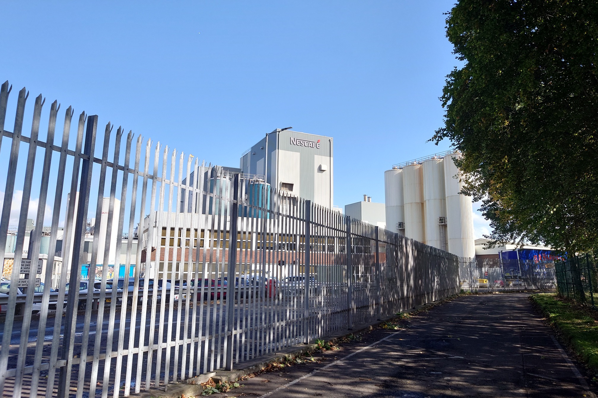 Behind a large metal fence, a large Nescafe factory towers into the blue sky