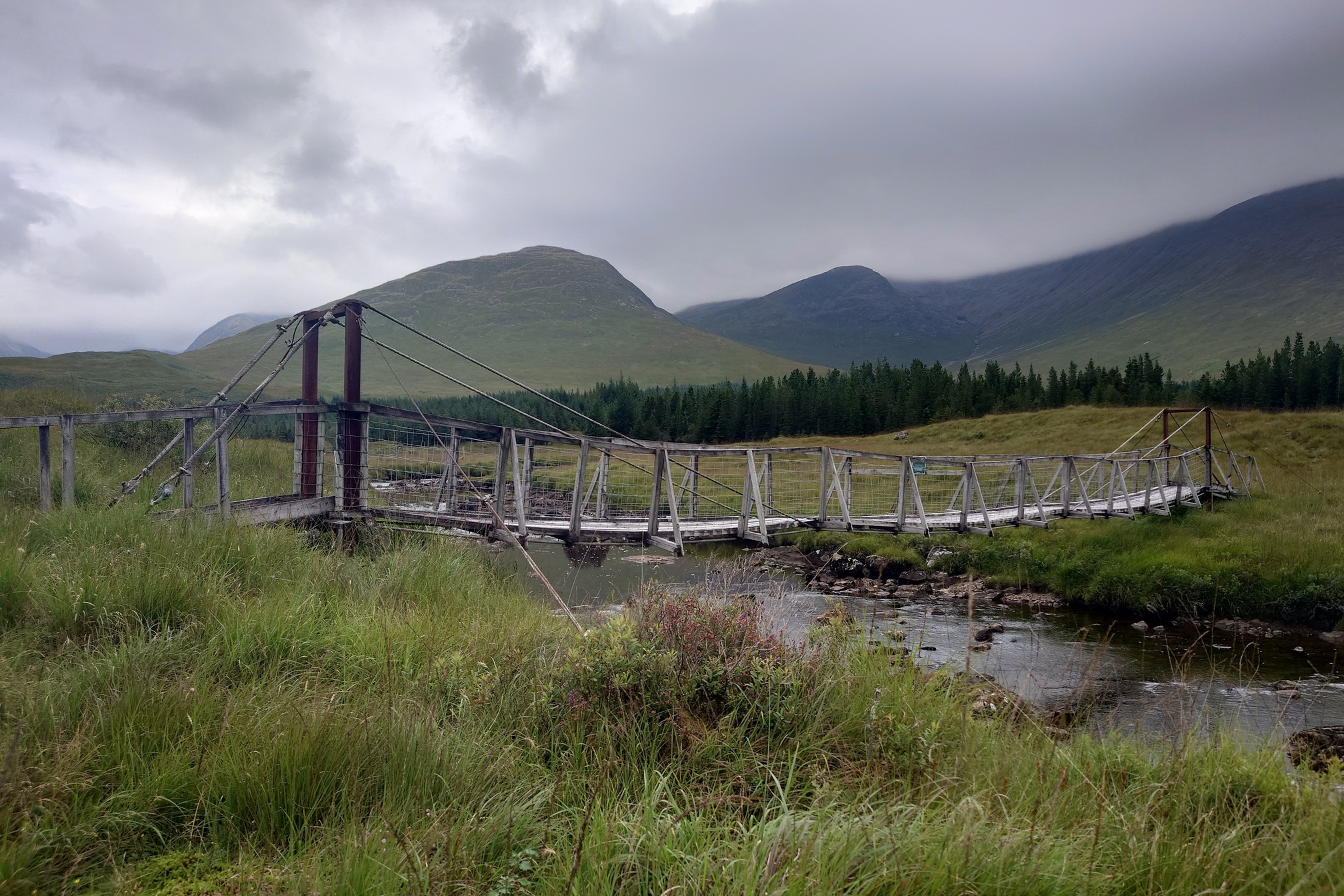 Crossing the river here is a wooden suspension footbridge. The piers on either side are brown with rust, and the rest of it is made of wood and looks very wobbly. I am sure it is perfectly safe.
