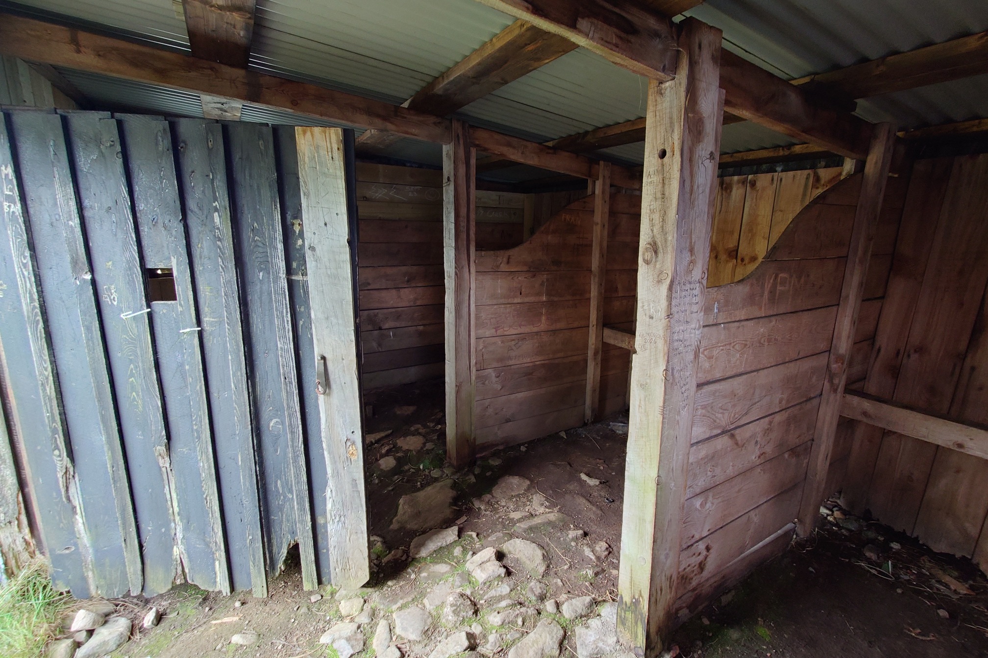 Inside, the ground has rough stone cobbles and is divided into three stalls by wooden partitions with curved edges. Grafitti has been written into the wood but you cannot make it out.