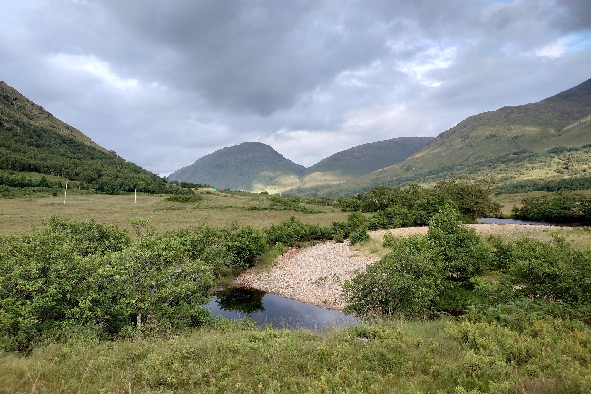 Looking down the glen, over a sandbar in the river. The valley bottom is much more wooded now.