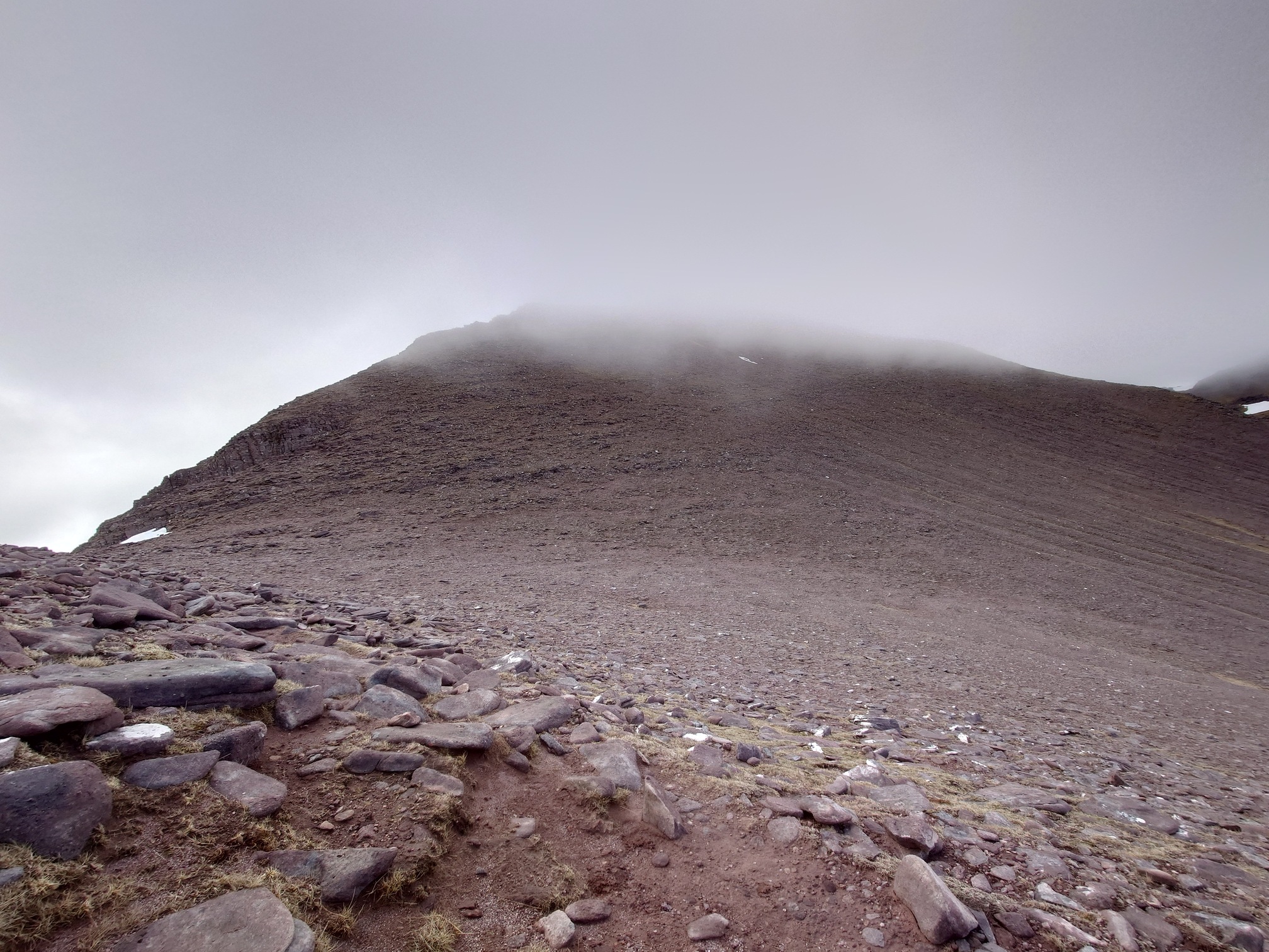 A steep rocky slope ascends into the cloud