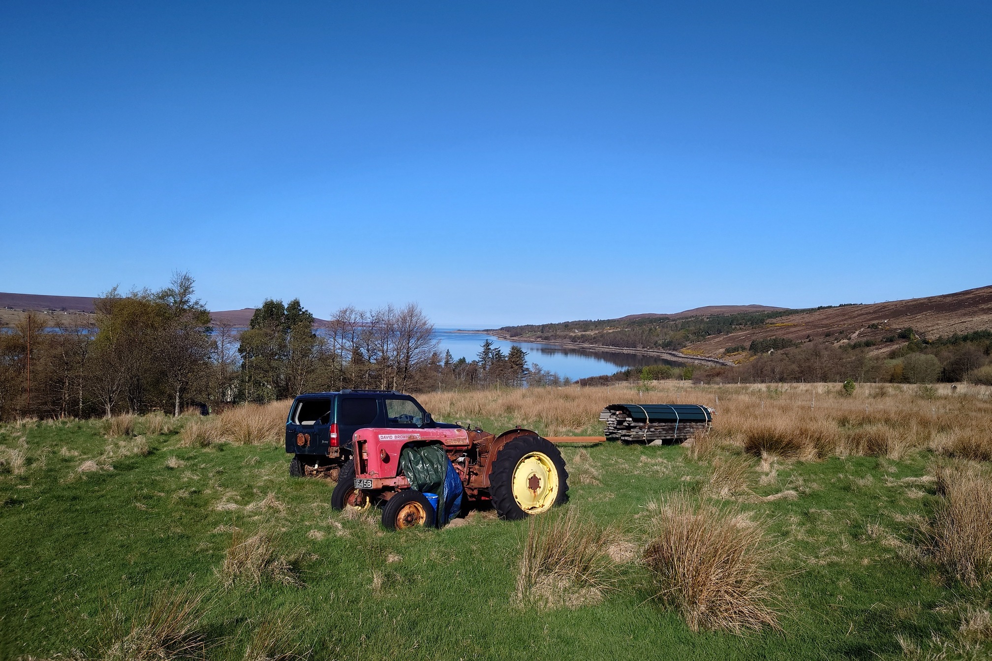 An old red tractor and a green landrover with no windows sit in a field
