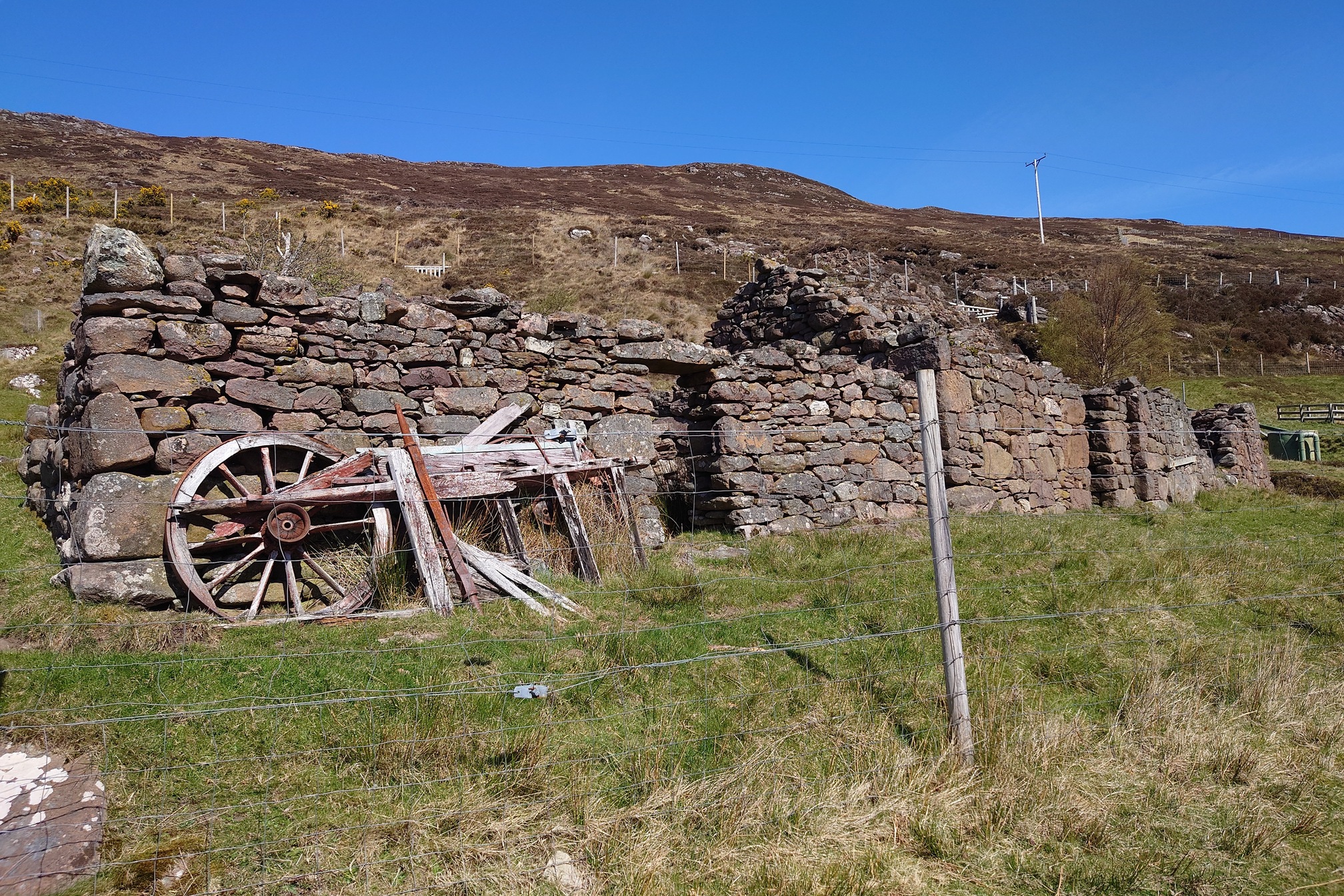 Old wood and a very old cart wheel are leaning against the roofless ruin of a very old cottage