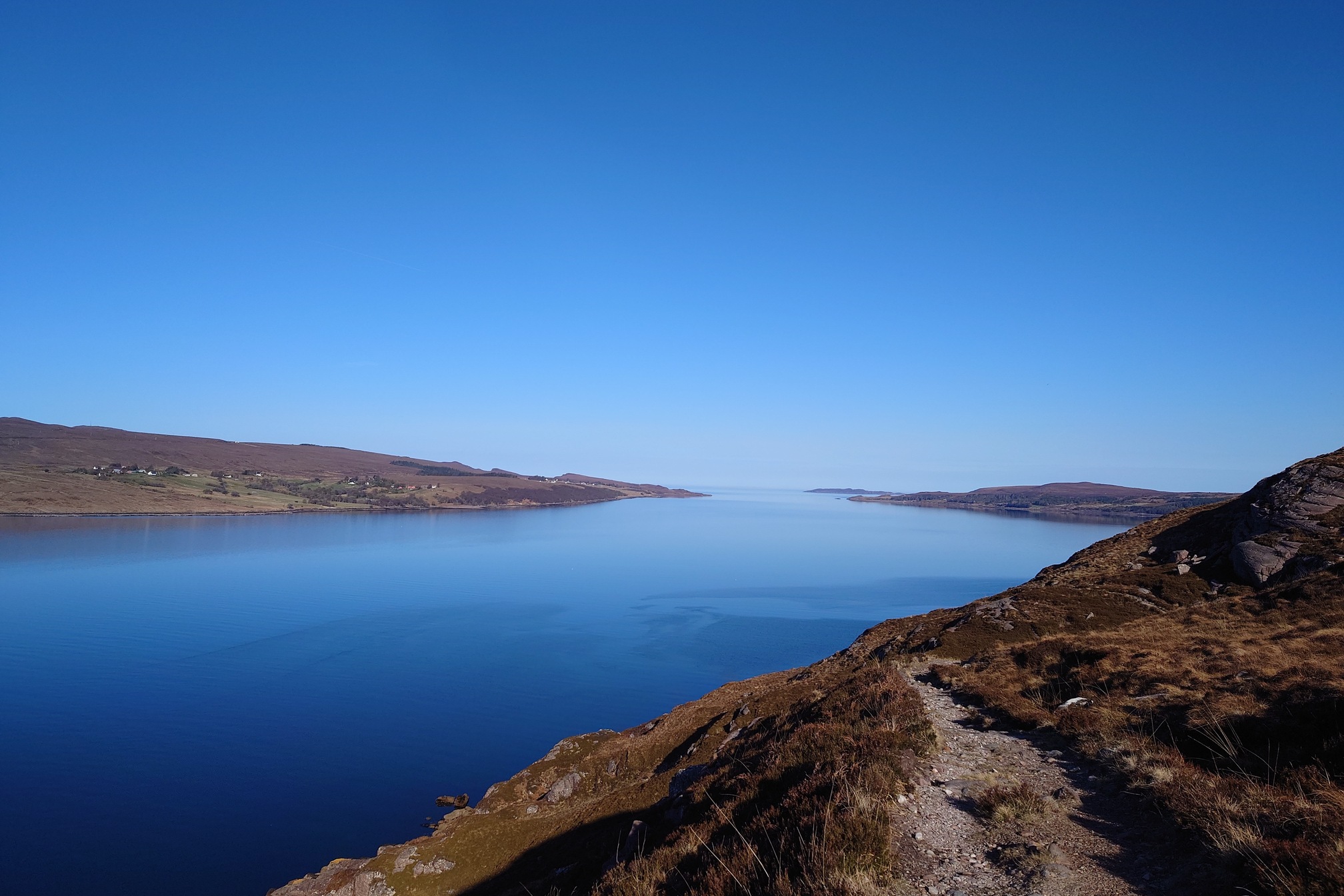 the narrow, rocky path cuts ahead across the ground sloping steeply away to Little Loch Broom, a large loch stretching to the horizon. It's as clear and blue as the sky.