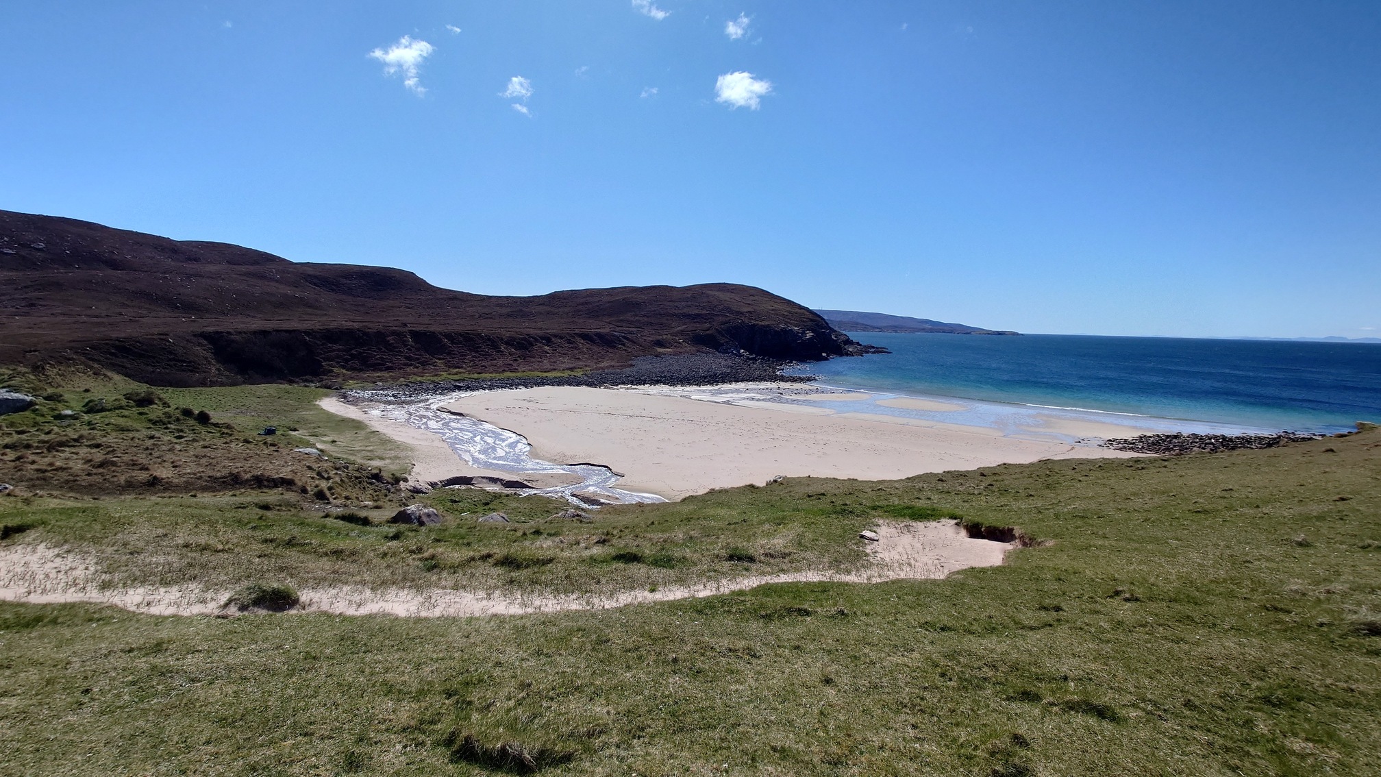A stream flows across a small sandy beach into the blue sea