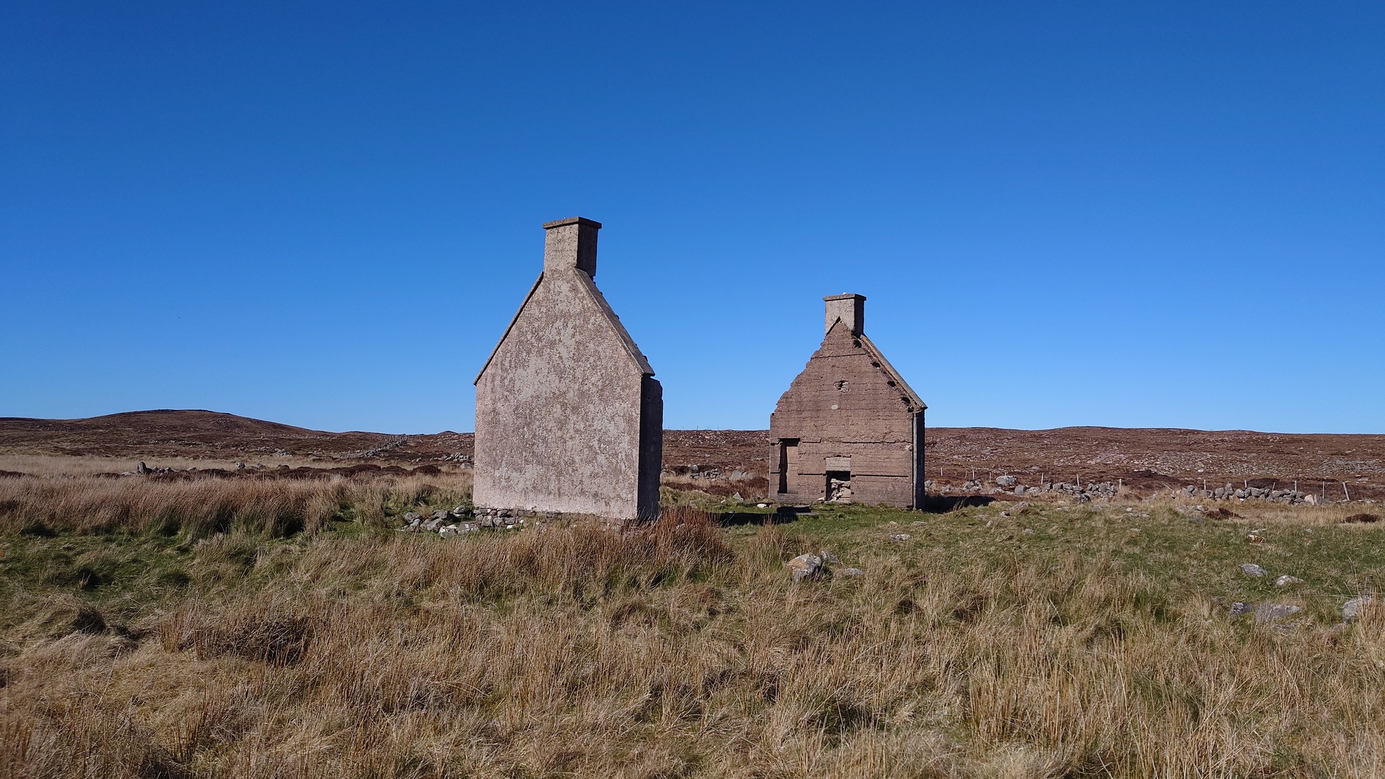 The gable ends of a two story house stand alone, facing each other, in a bare, grass landscape