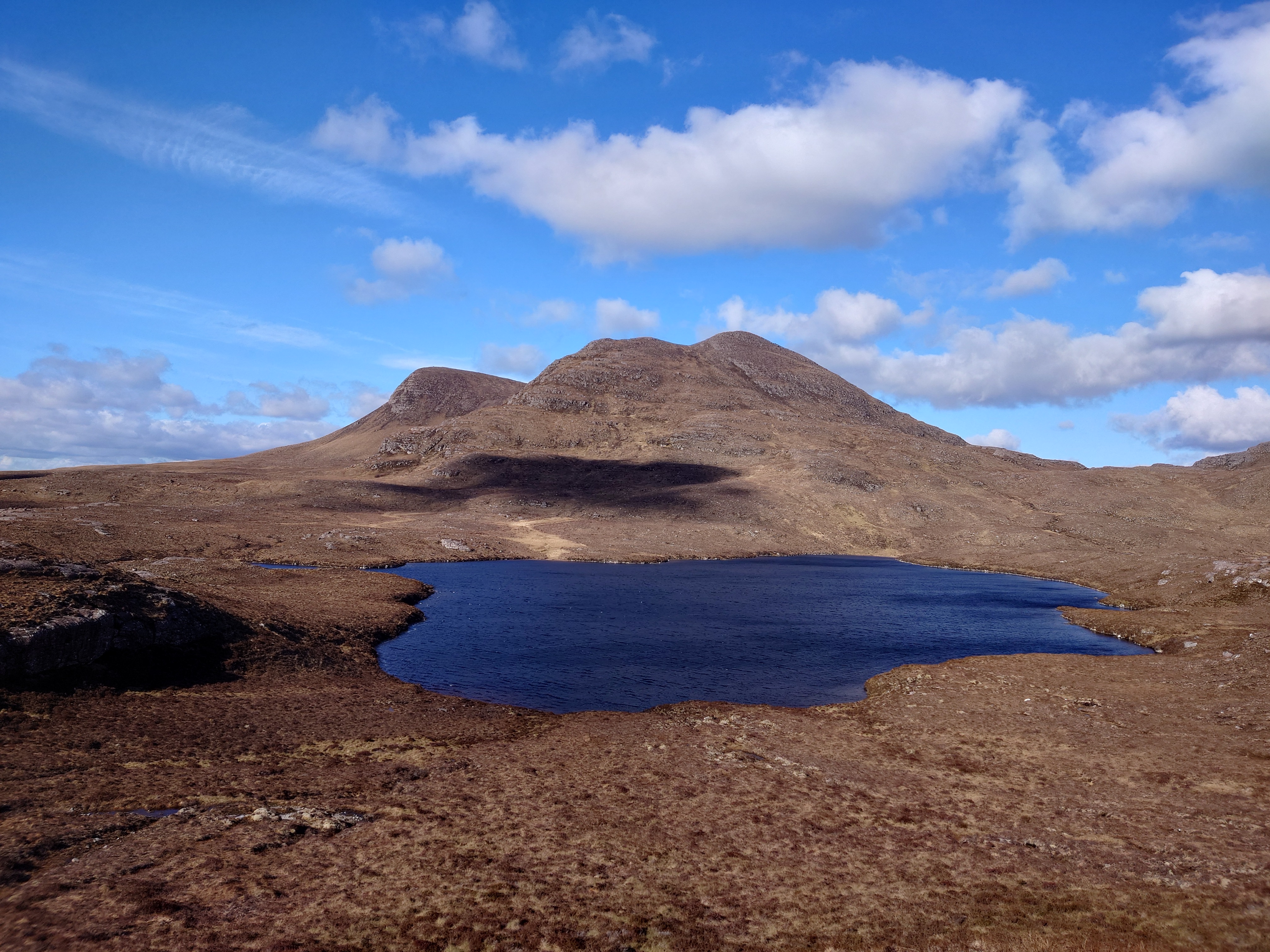 A little blue loch sits in a dip under the summit of Beinn Ghobhlach