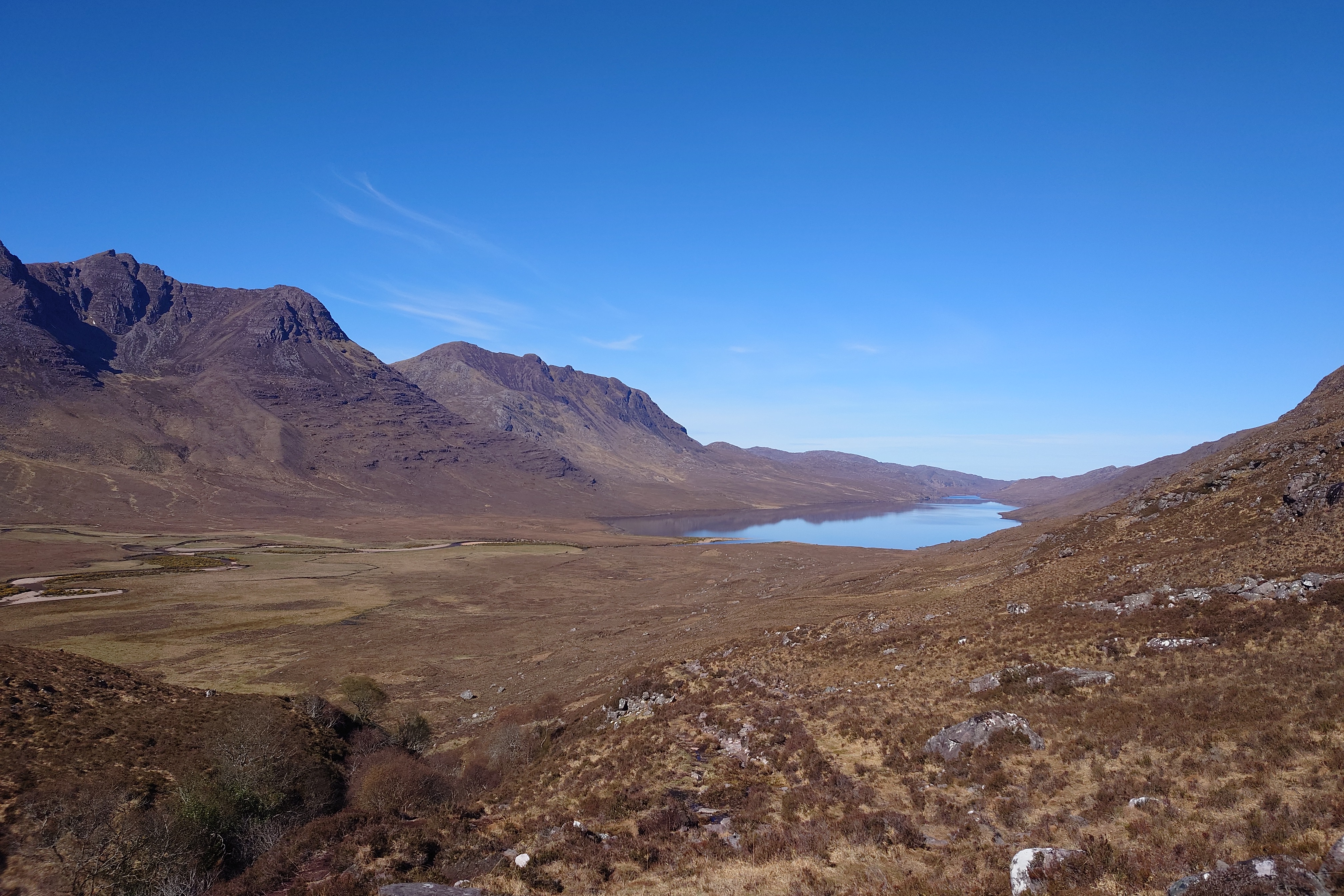 The vase landscape, a loch sits at the bottom of a curving valley bounded by mountains. A very brown/yellow scene of mostly heather and dry grasses. Not a single tree.