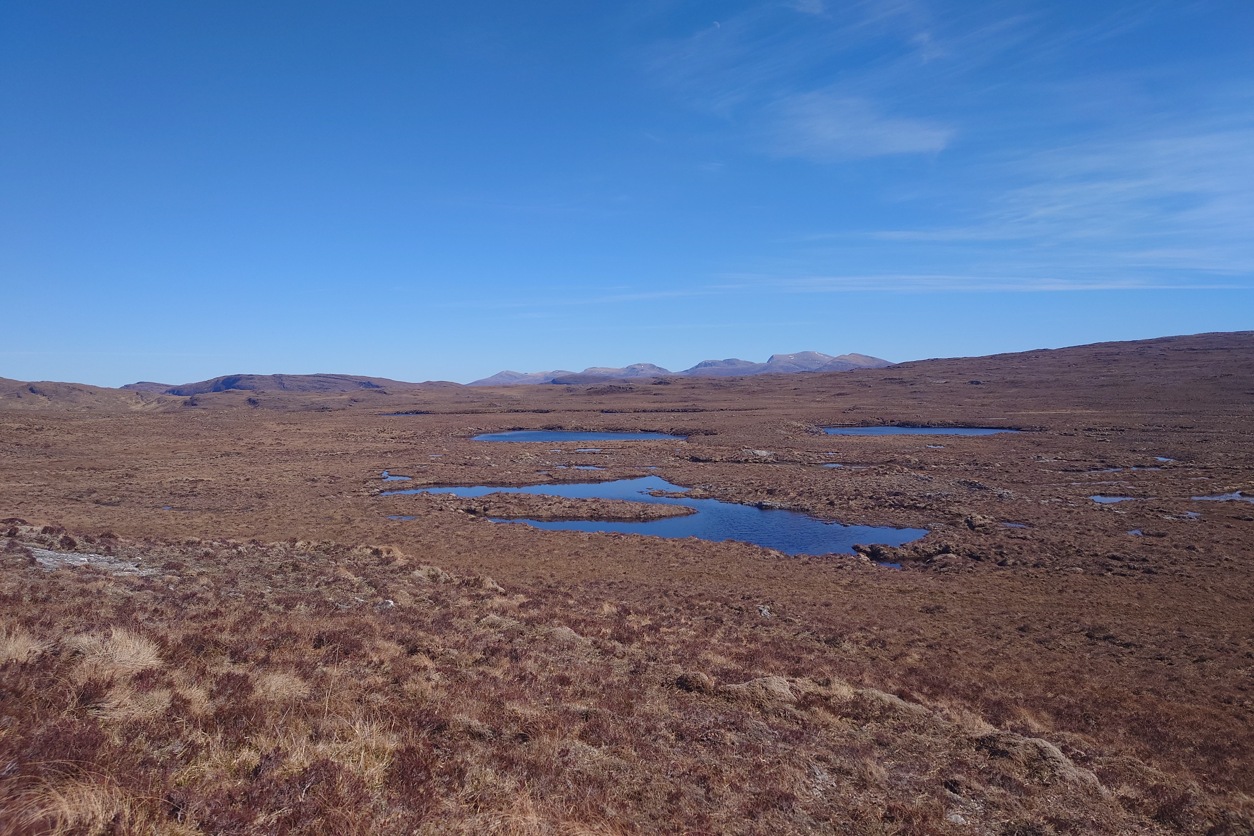Lochain Dubh, a collection of small blue waterbodies sitting in an expanse of barren, flat heather. On the far far horizon - more mountains.